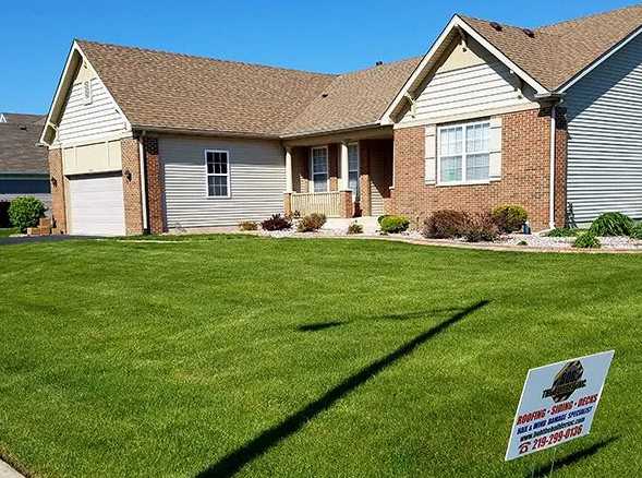 House with brick and tan siding, lush green lawn, and sign.