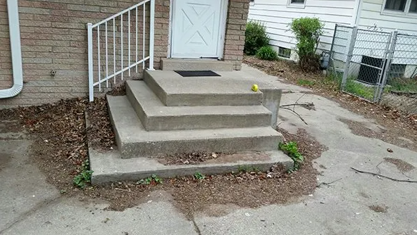Concrete steps leading to a white door, with a white railing to the left.