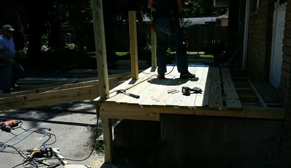 Workers constructing a wooden deck with railings; tools and lumber visible.
