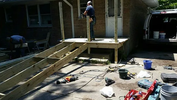 Man building a wooden deck with a ramp. Tools and materials are scattered around the construction site.