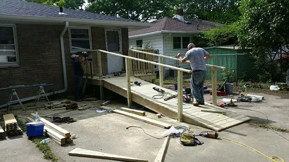 Two people building a wooden wheelchair ramp next to a house on a sunny day.
