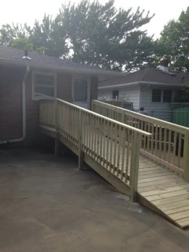 Wooden ramp leading up to a house entrance. The ramp has railings on both sides. Cloudy sky.