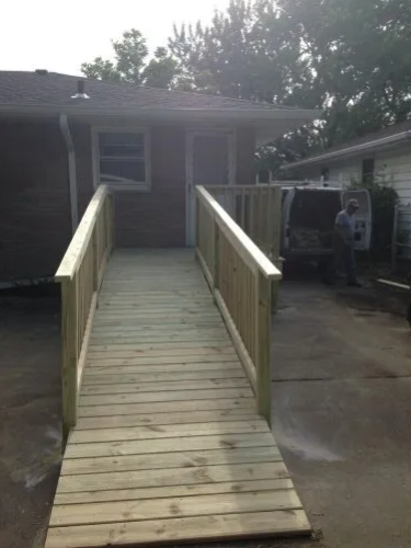 Wooden ramp with railings leading to a doorway. A person stands near a white van.