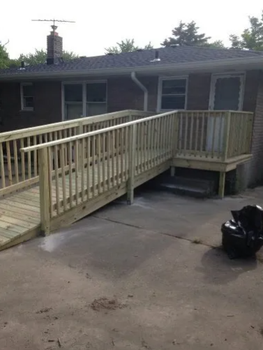 Wooden ramp and deck providing accessible entry to a brick house. Includes handrails and steps.
