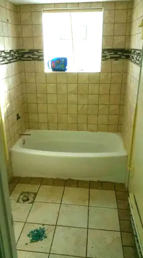 Bathroom with white bathtub, tiled walls and floor, and window with a cup.