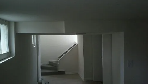 Interior hallway with stairway in the distance, bathed in daylight, with white walls and a window.