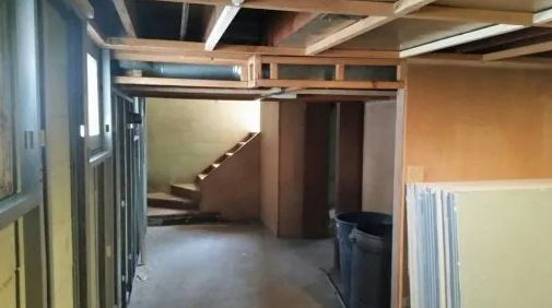 Basement under construction, exposed beams, drywall, unfinished staircase.