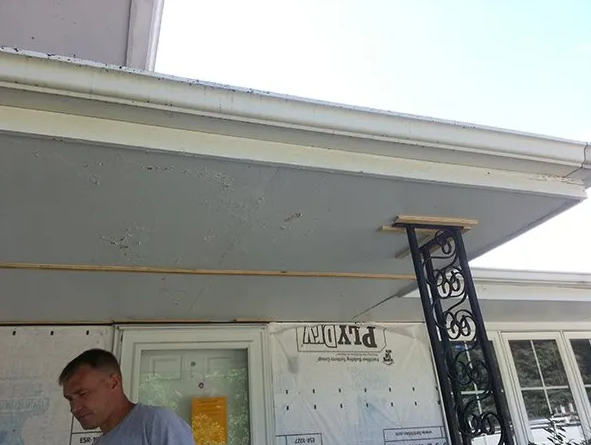Man working on a porch ceiling under a blue-gray overhang with a decorative black support.