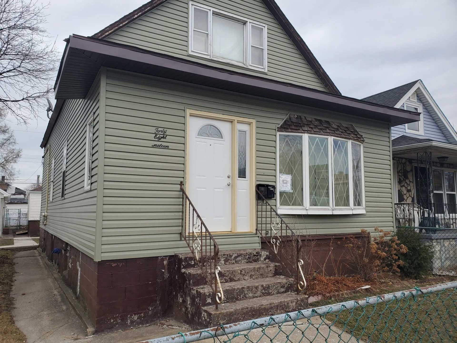 House with green siding, brown trim, white door, and bay window. Front steps lead to the entrance.