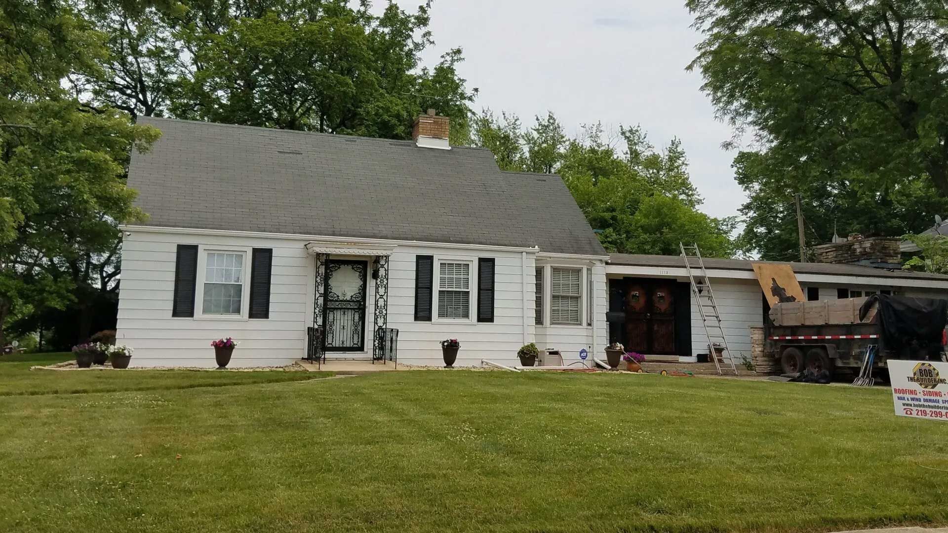 Dilapidated house with peeling siding, set on a grassy lot, sidewalk in front, overcast sky.