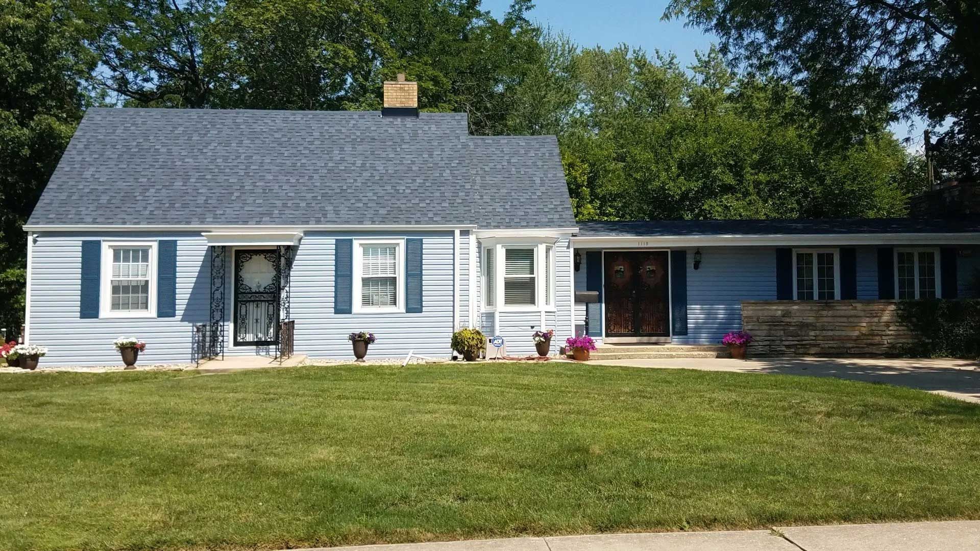 House with green siding, brown trim, white door, and bay window. Front steps lead to the entrance.