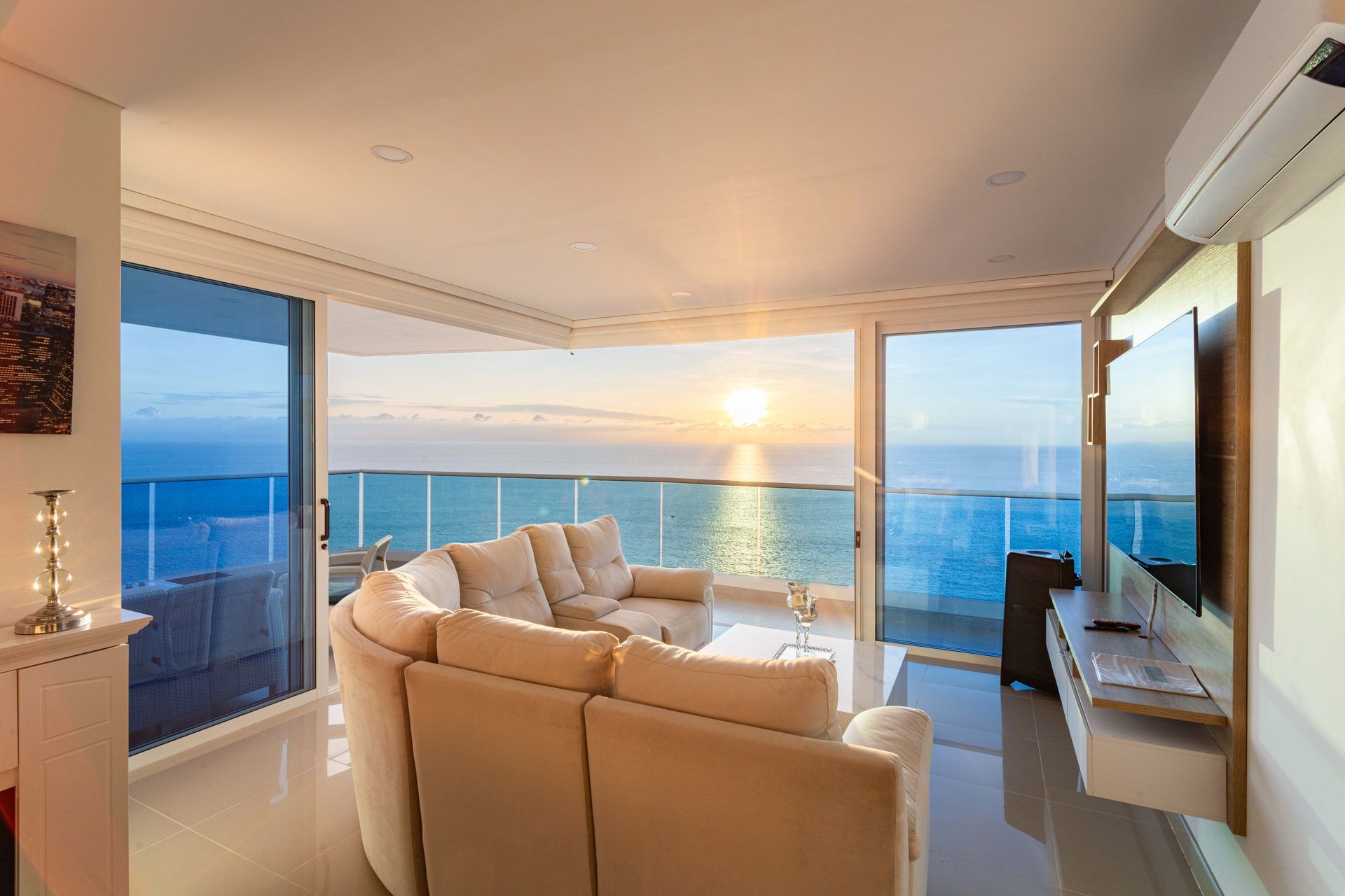 Modern living room with beige sofas overlooking an ocean sunset through floor-to-ceiling windows