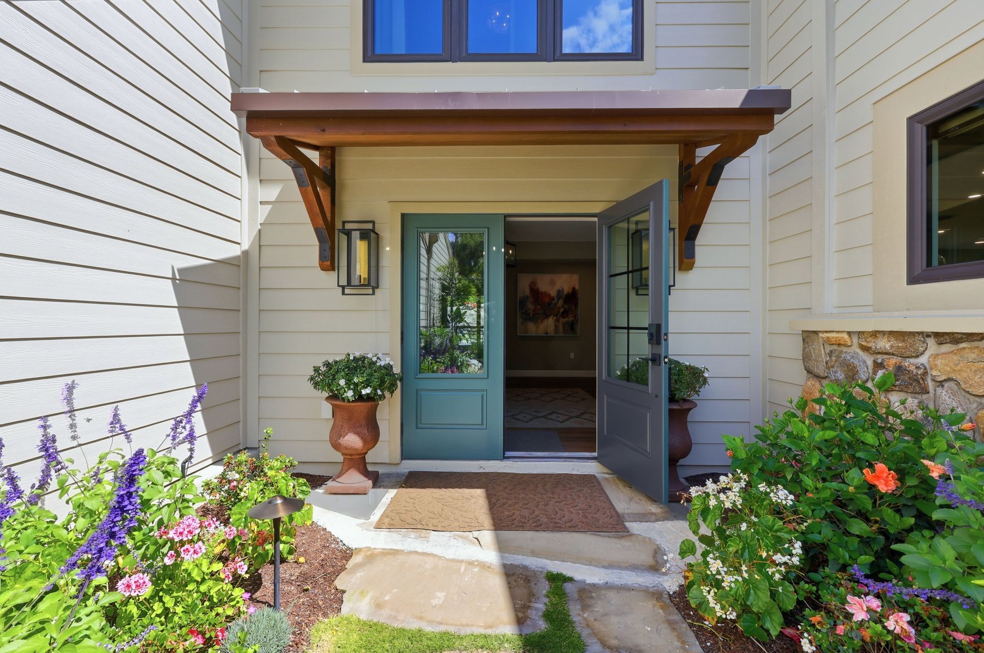 Front entry of a house with teal double doors, stone path, potted plant, and blooming flowers