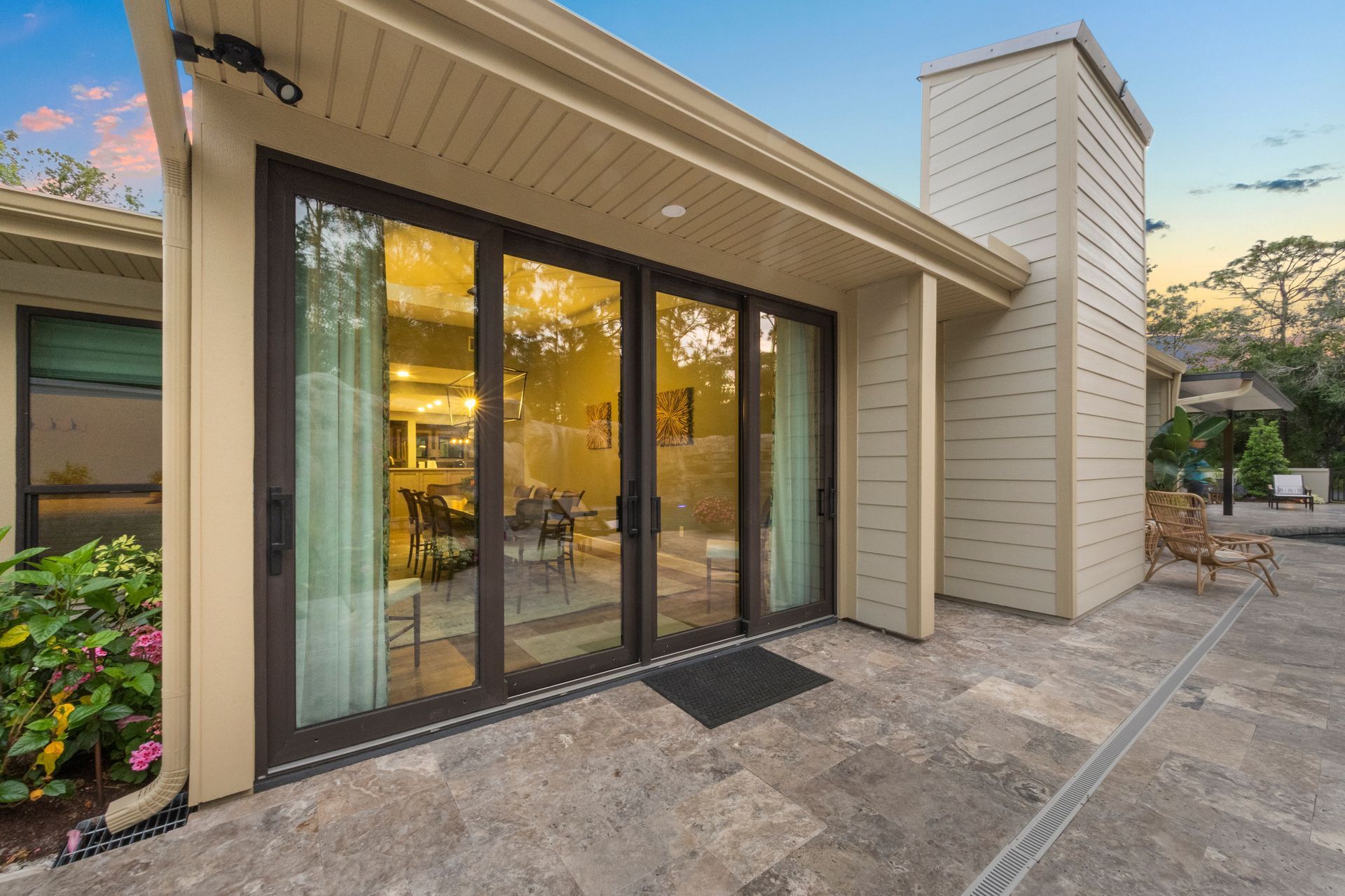 Exterior of a modern home with large sliding glass doors and a patio at sunset