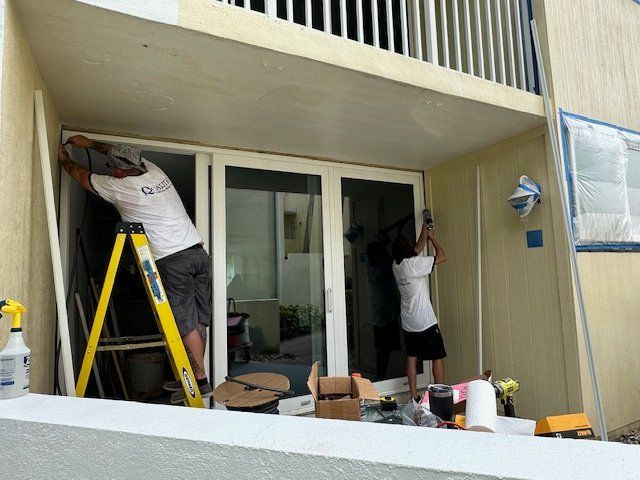 Two men are working on a sliding glass door on a balcony.