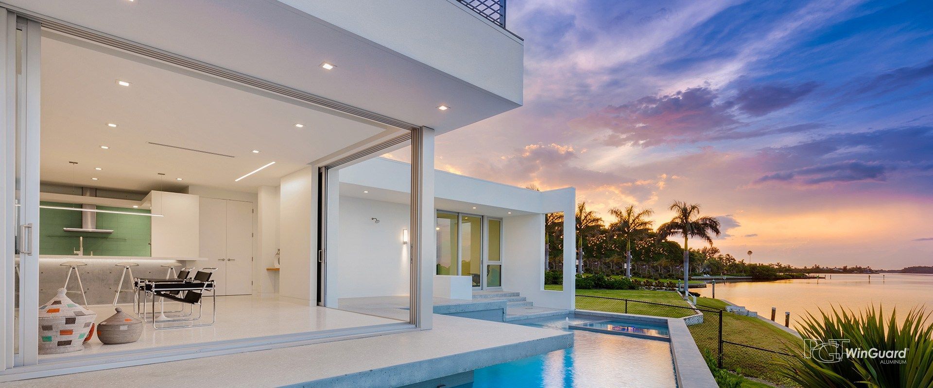 A modern house with a swimming pool and a view of the ocean at sunset.