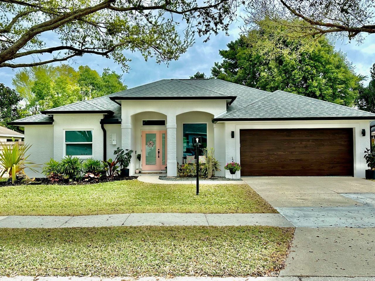A white house with a brown garage door and a pink door