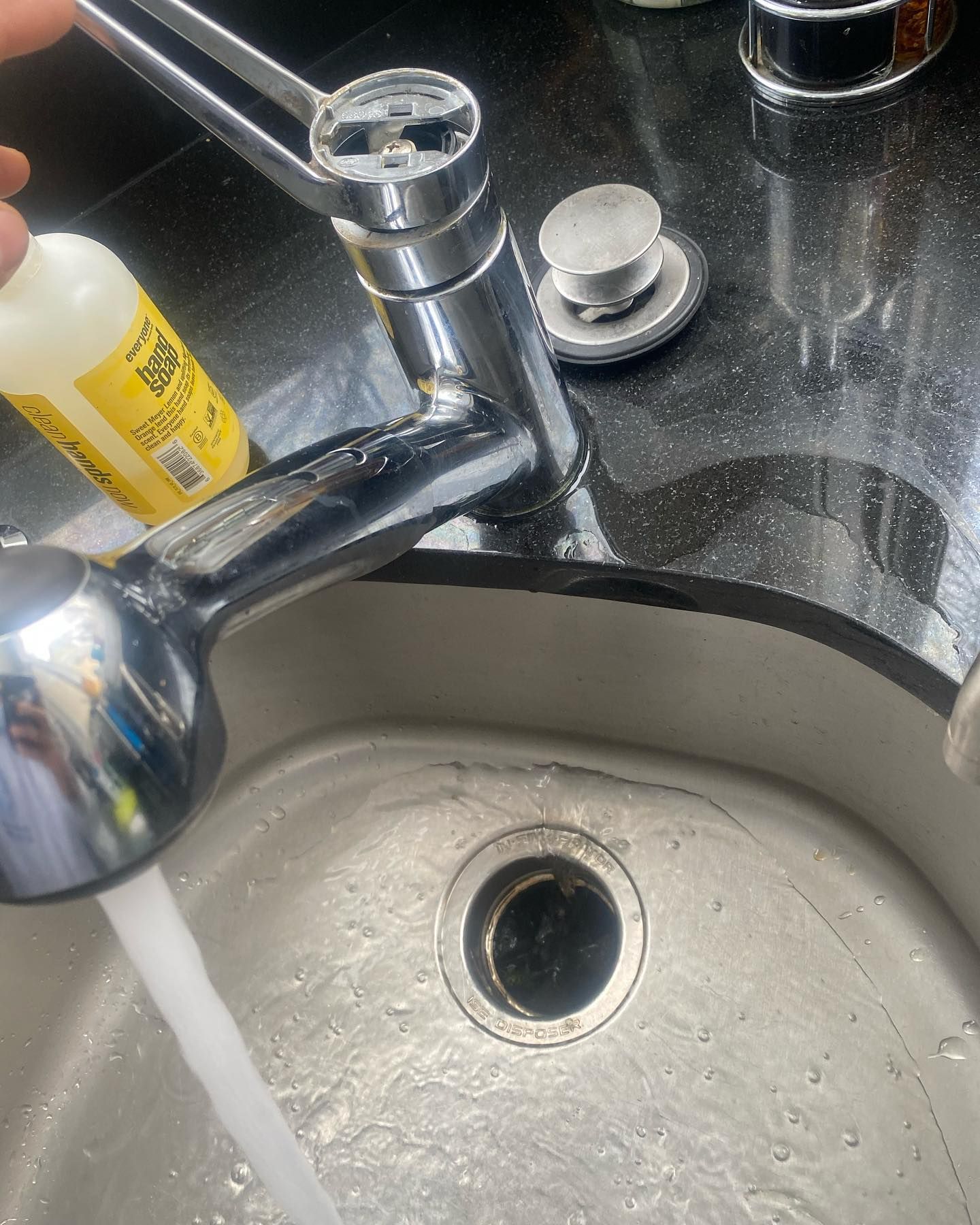 Faucet with running water, black countertop, stainless steel sink, drain visible.