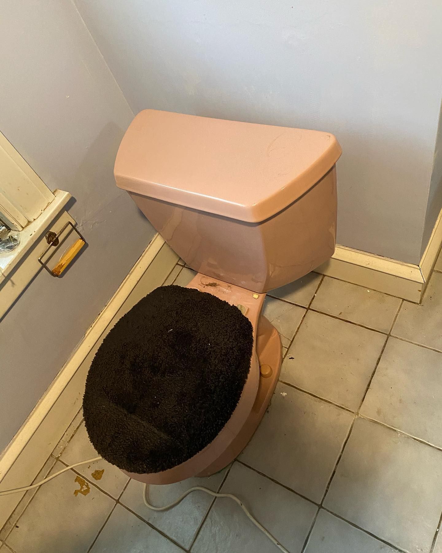Pink toilet with a black fuzzy seat in a tiled bathroom.