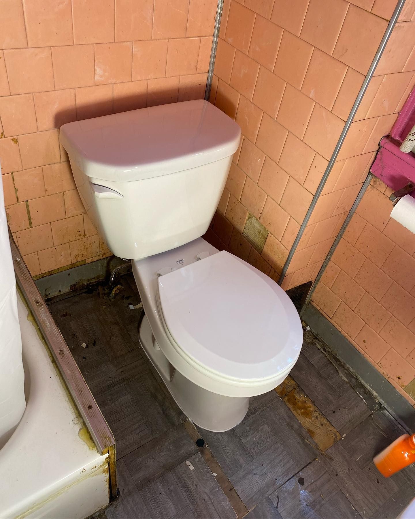 White toilet in a bathroom with pink tiled walls and worn, brown flooring.