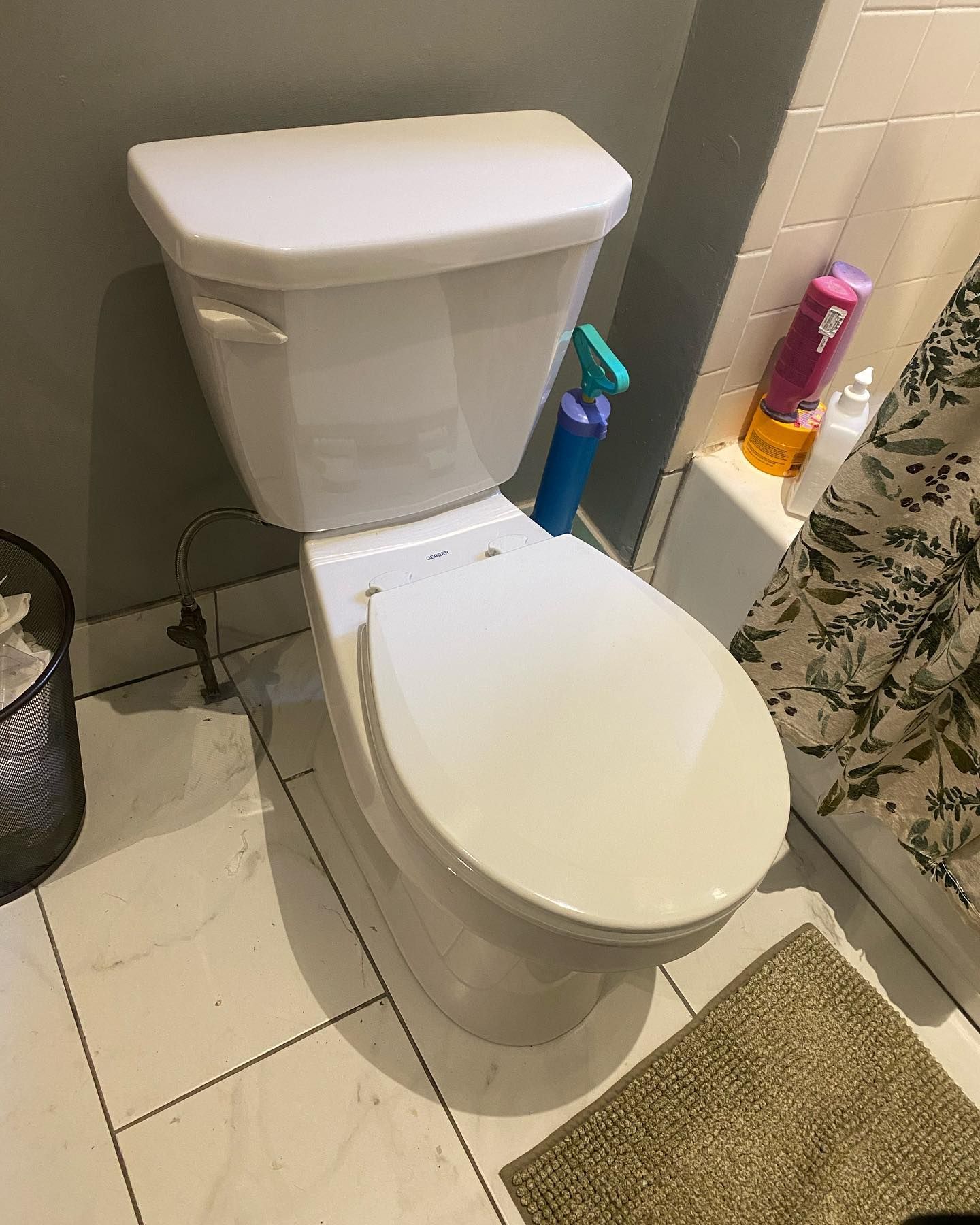 White toilet in a bathroom with gray walls, white tiles, and toiletries on the tank.