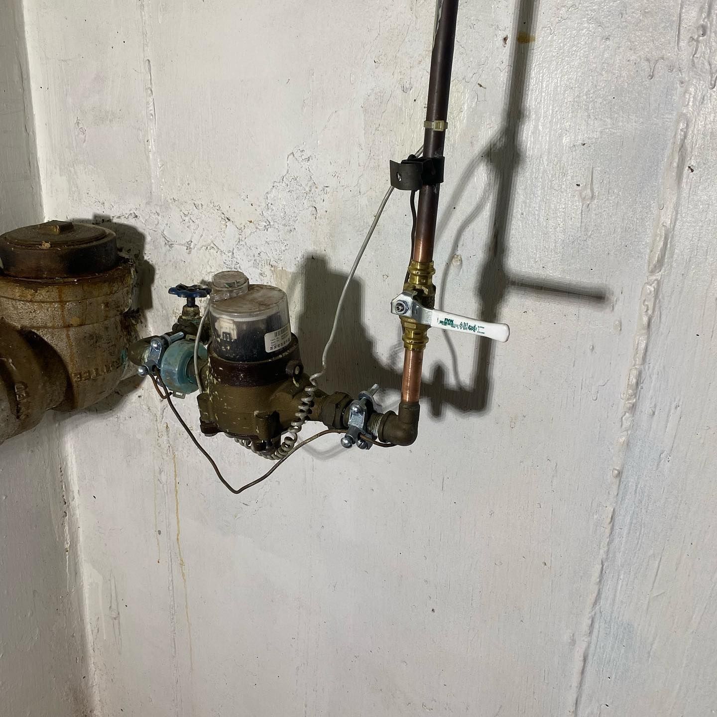 Water pipes and a meter attached to a concrete wall. A metal valve is open.