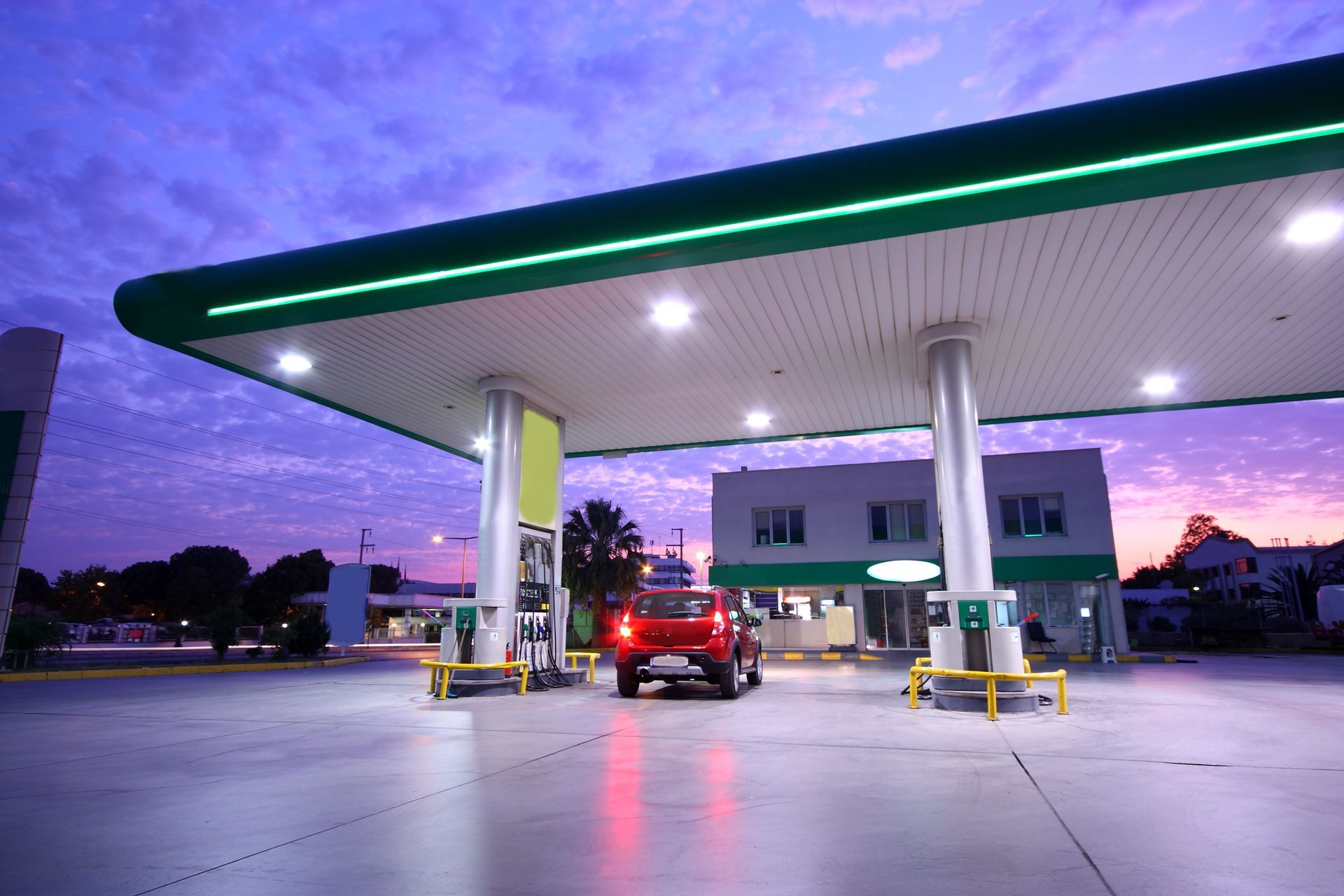 Gas station at dusk with a red car under a lit green canopy