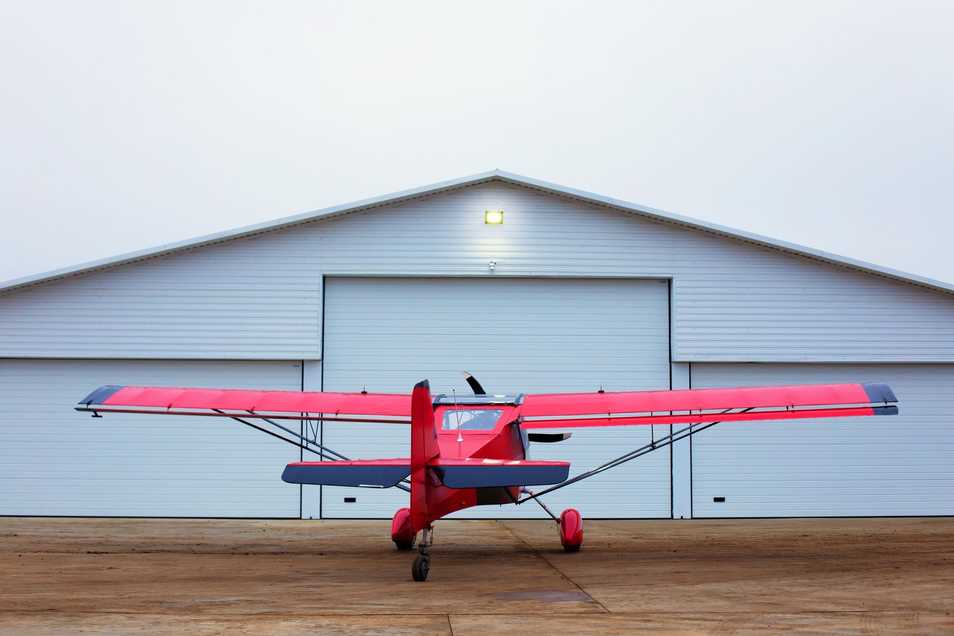 Pink airplane parked in front of a white hangar on a dirt runway