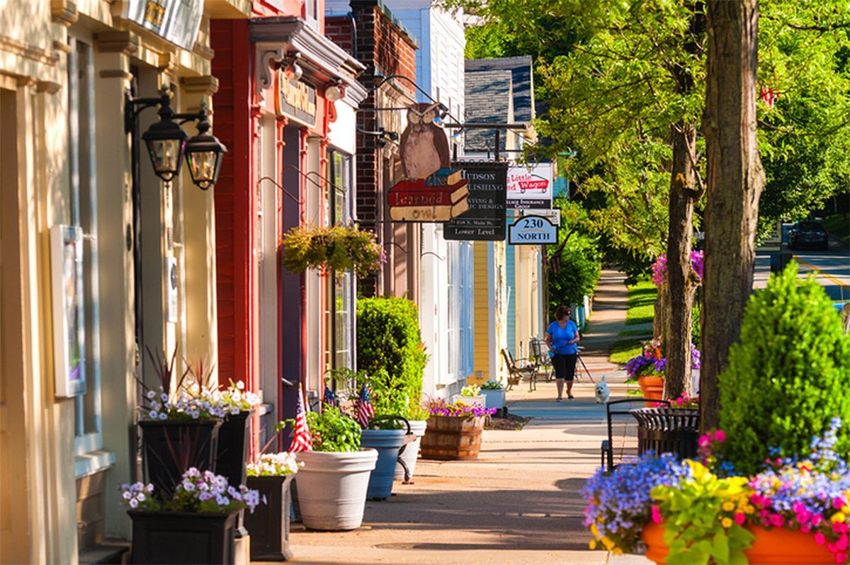 Sunny sidewalk lined with colorful potted flowers and quaint storefronts on a charming street