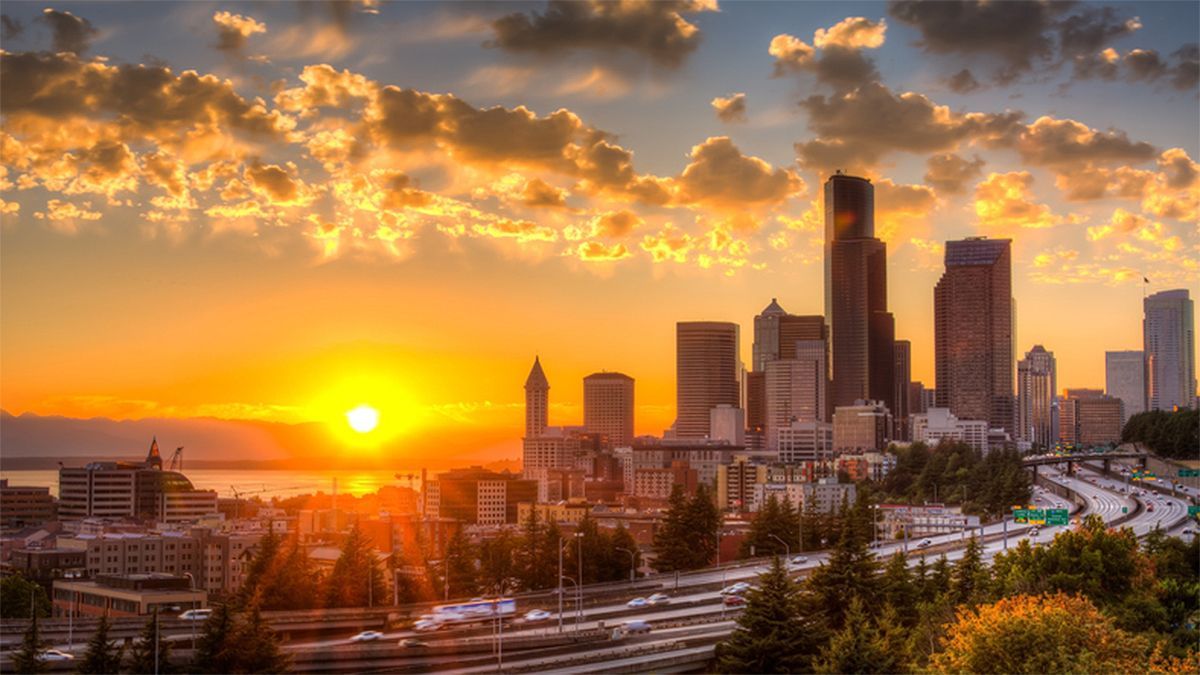 Sunset over a city skyline with glowing clouds and the sun near the horizon