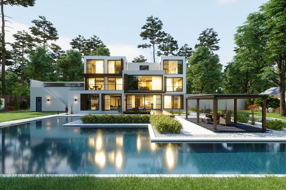 Modern luxury house with large pool, glass railings, and landscaped trees at dusk.