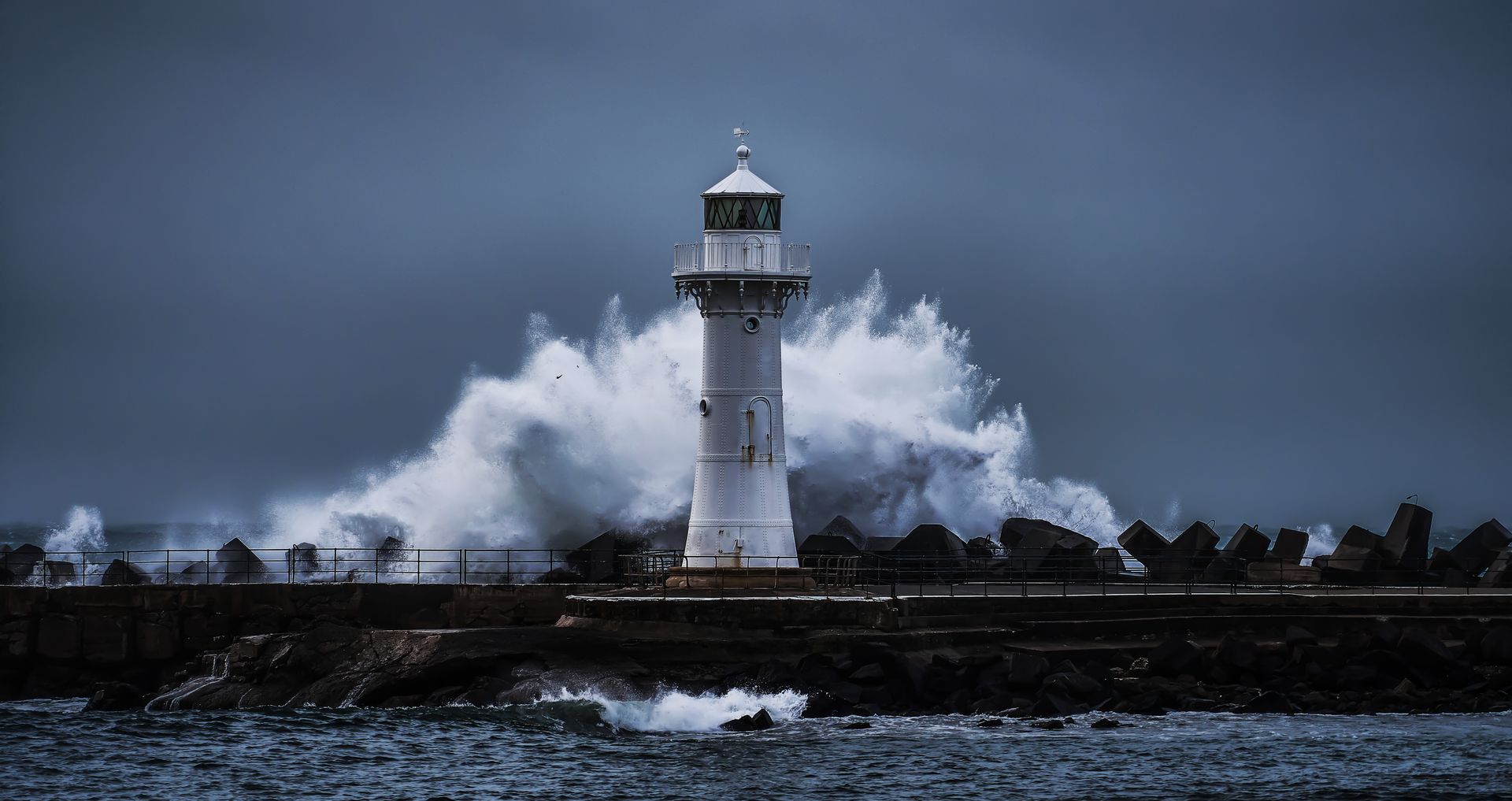 Lighthouse amid crashing waves on a stormy, dark shoreline at dusk