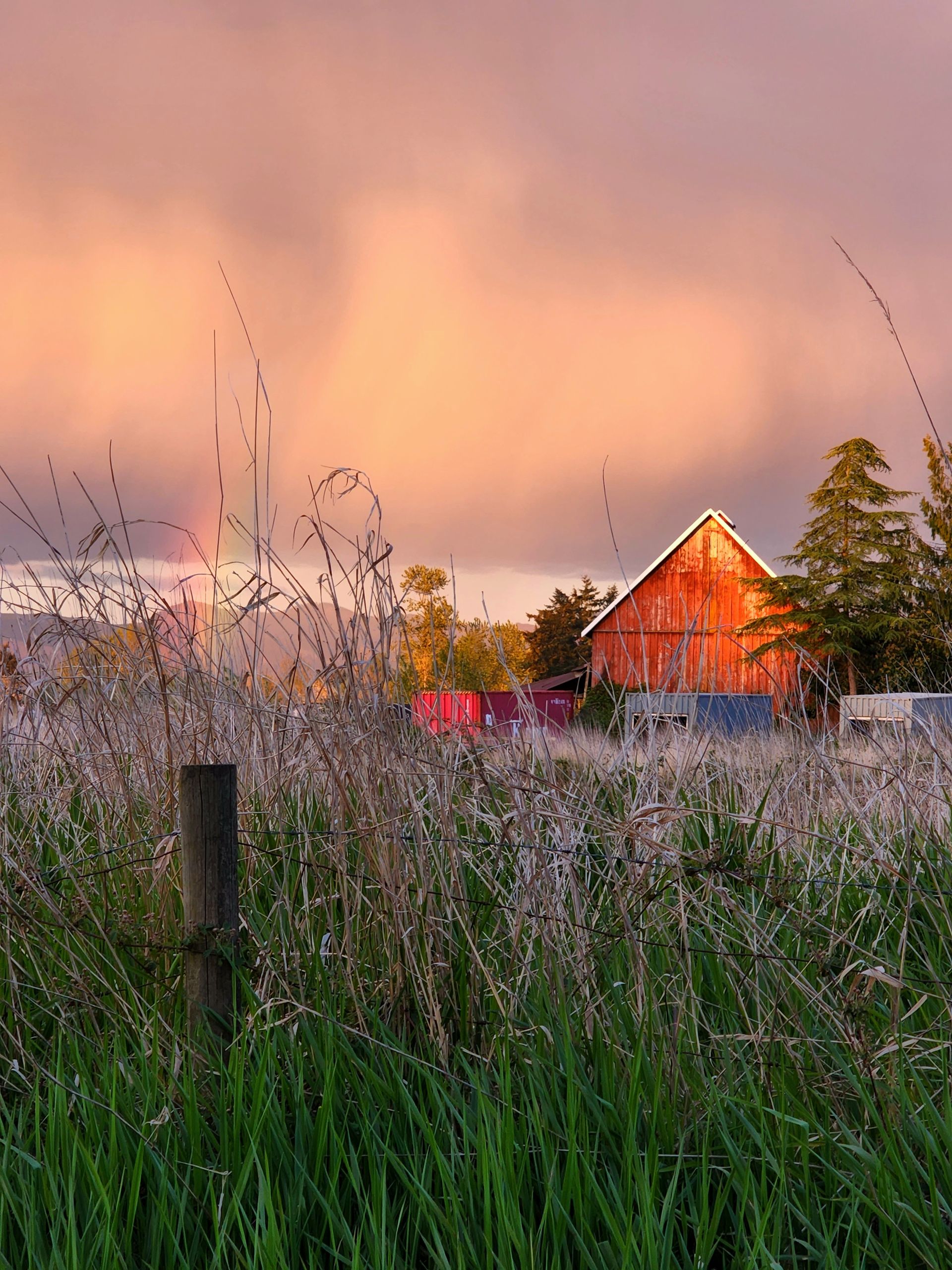 Orange barn in a frosty field at sunset beneath a pink-orange sky.