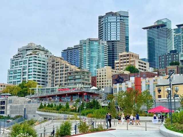 City waterfront promenade with people, modern high-rises, and blue sky.