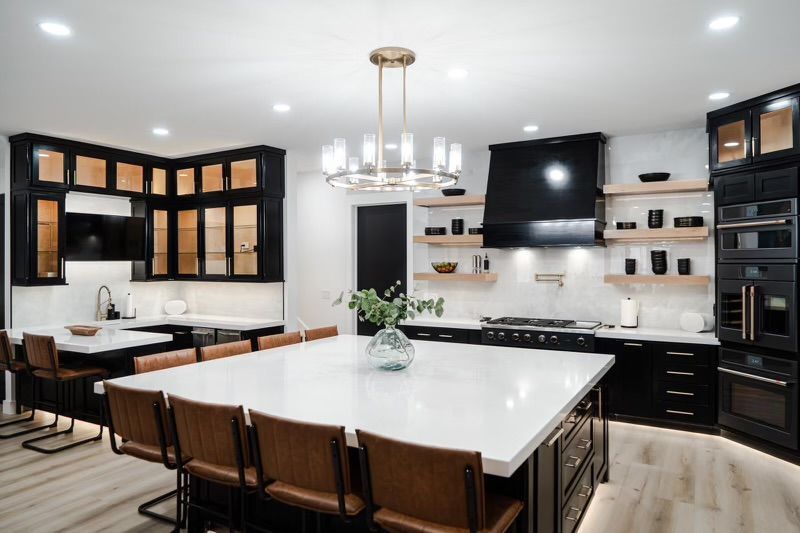 A kitchen with black cabinets, white counter tops, and a large island.