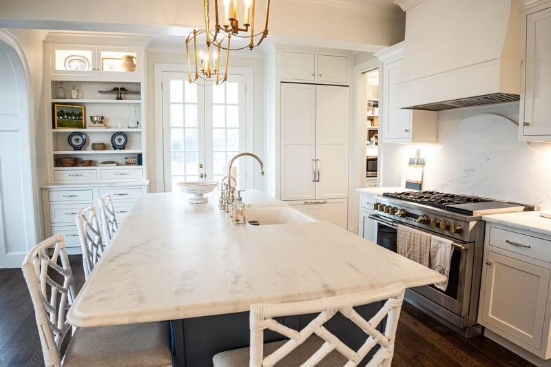 A kitchen with white cabinets, a large island, a stove, and a sink.