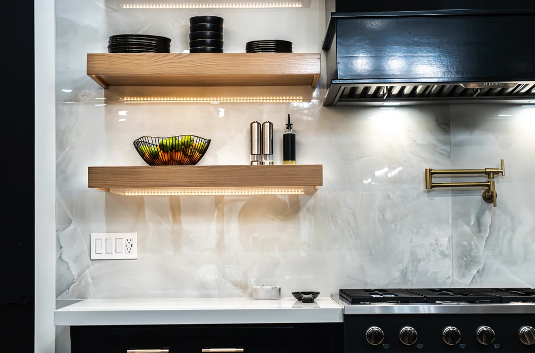 A kitchen with a stove , shelves , and a hood.