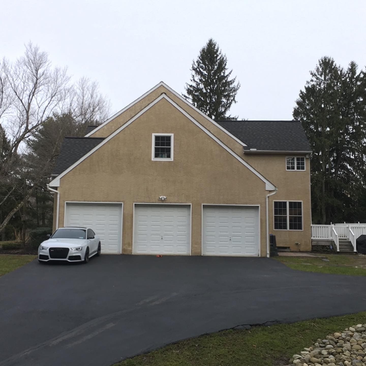 A car is parked in front of a house with three garage doors
