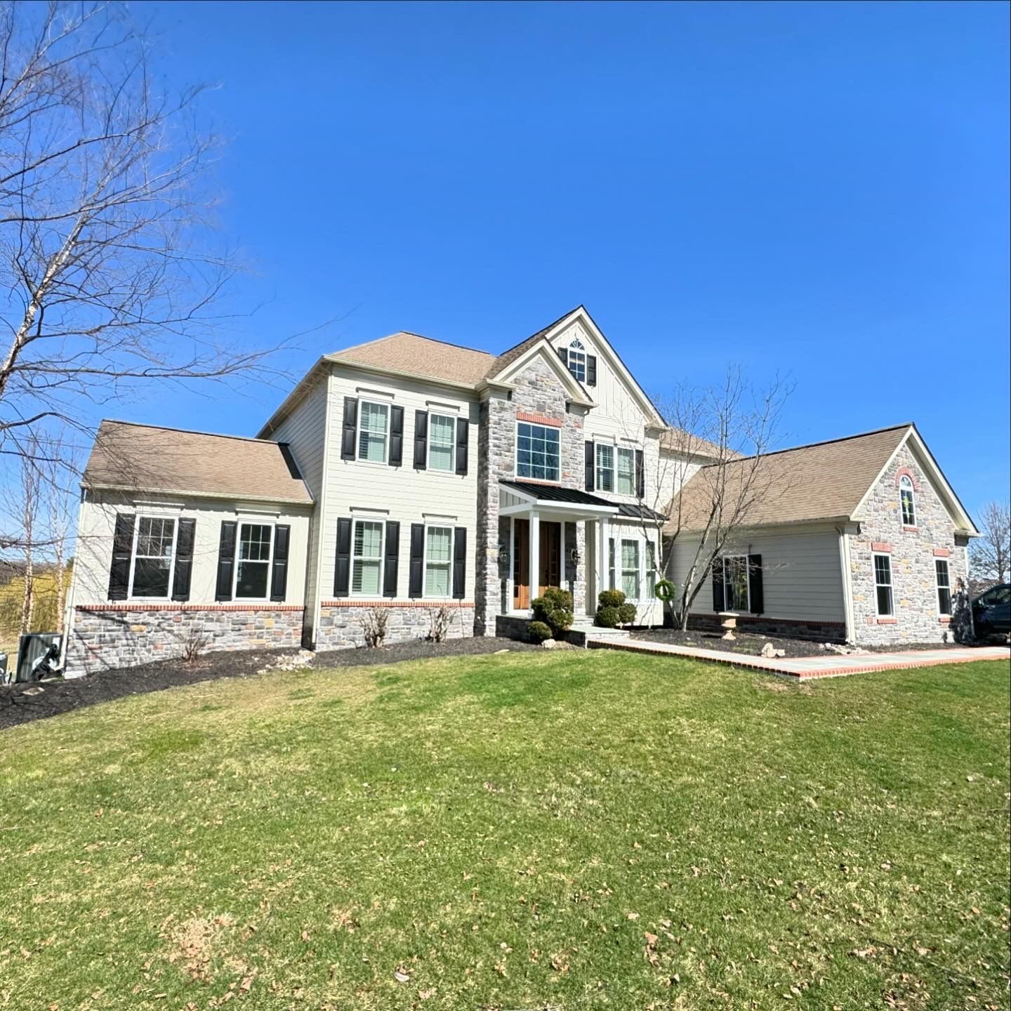 A large white house with a brown roof is sitting on top of a lush green field.
