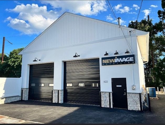 A white building with black garage doors and a sign that says newimage