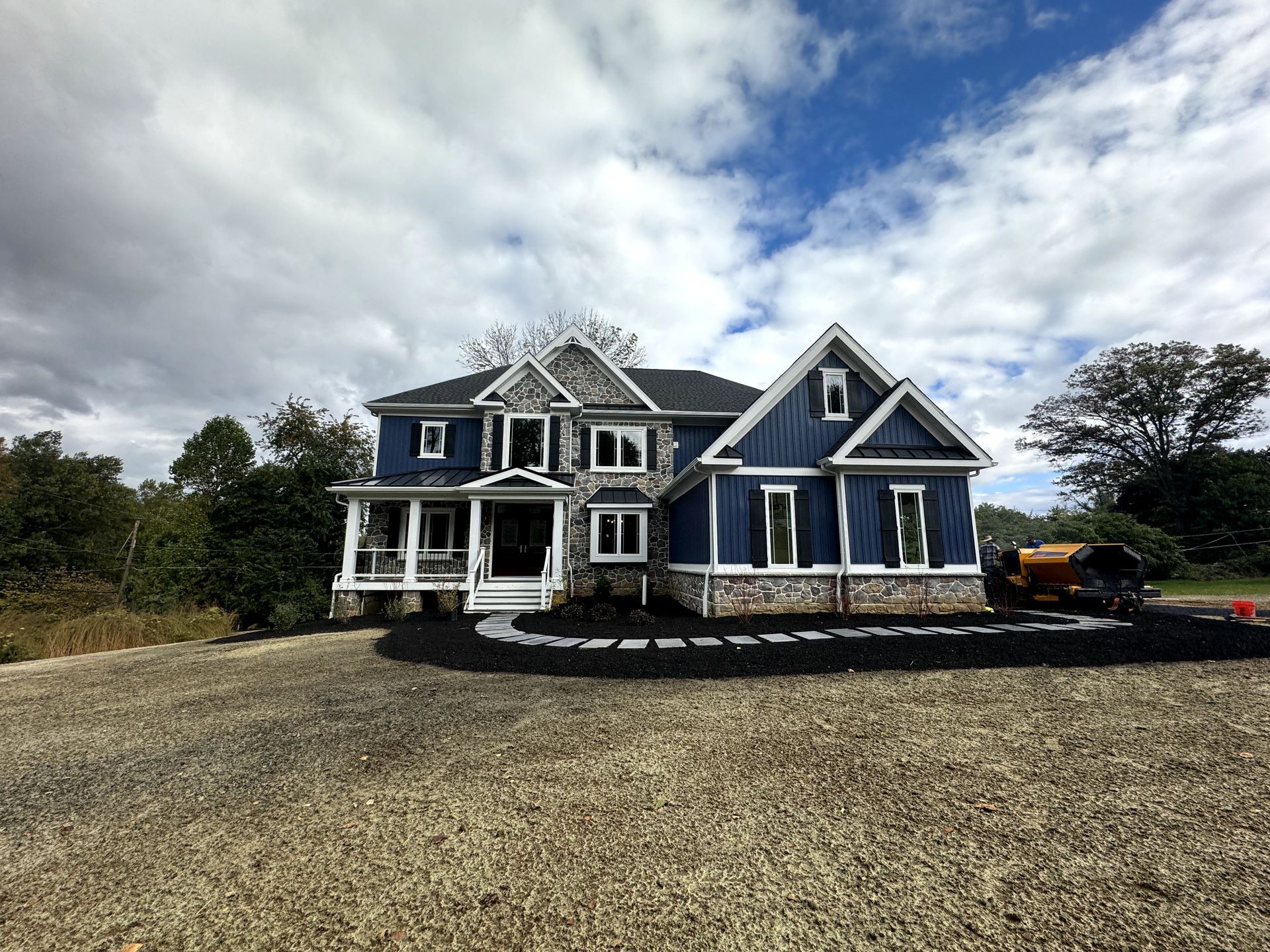 A large blue and white house is sitting on top of a gravel driveway.