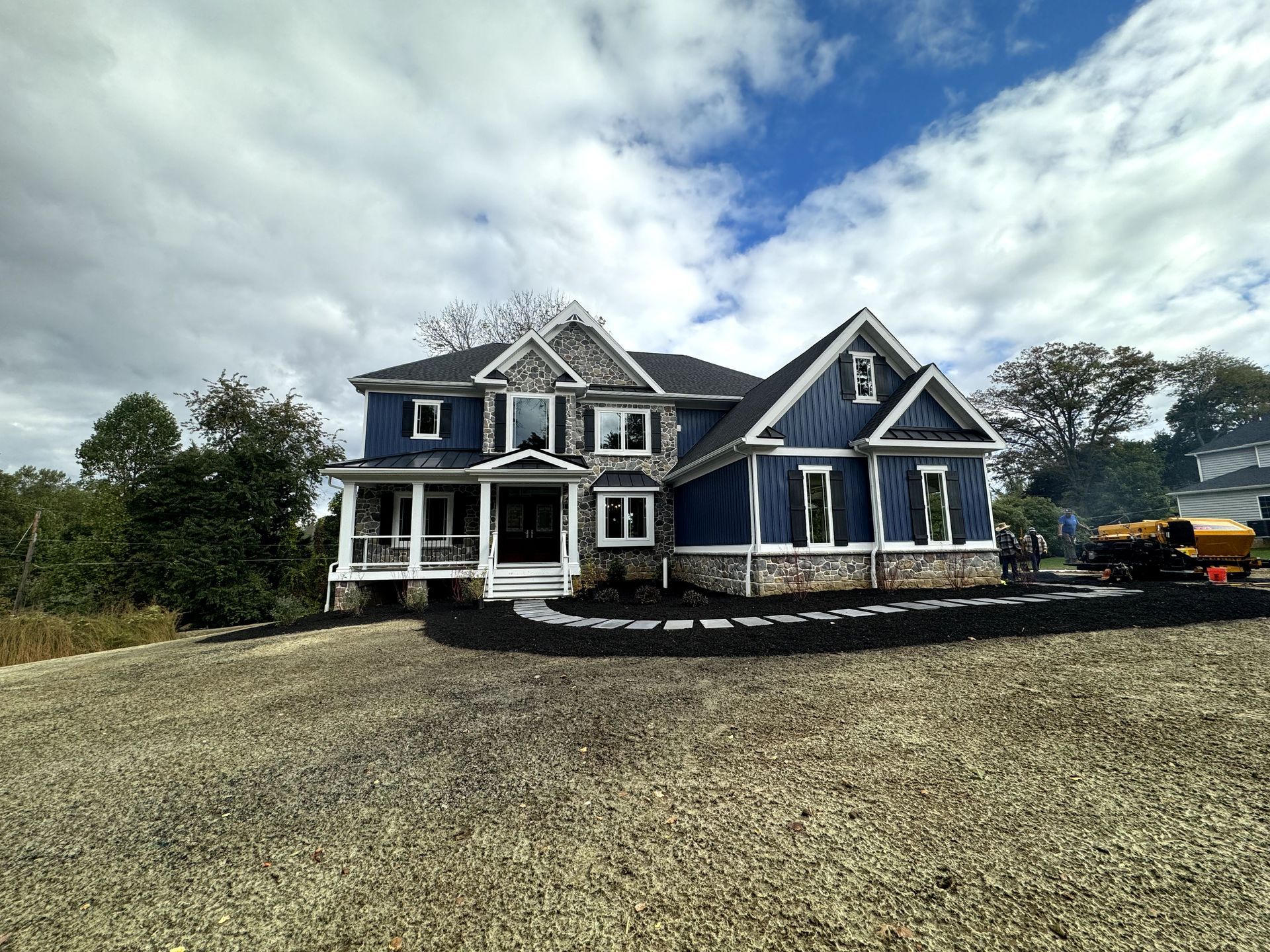 A large blue house is sitting on top of a gravel driveway.