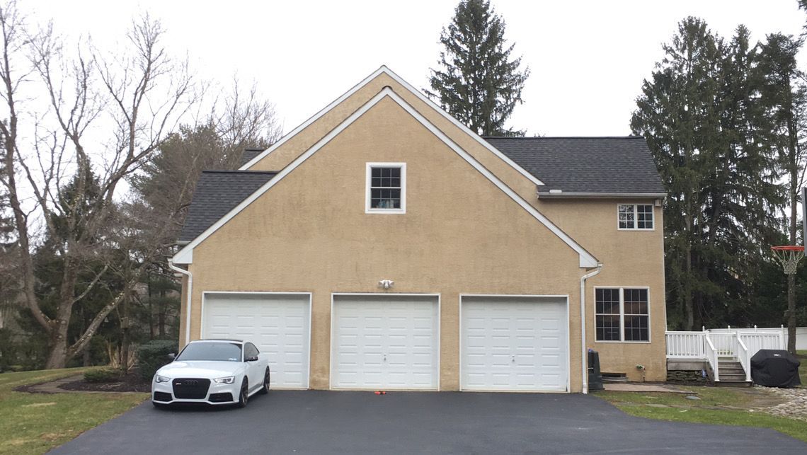 A car is parked in front of a house with three garage doors