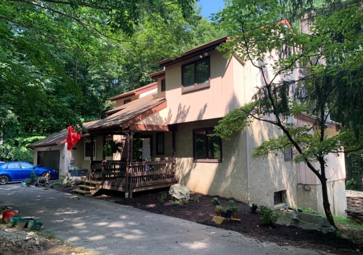 A large house with a red flag on the porch is surrounded by trees.