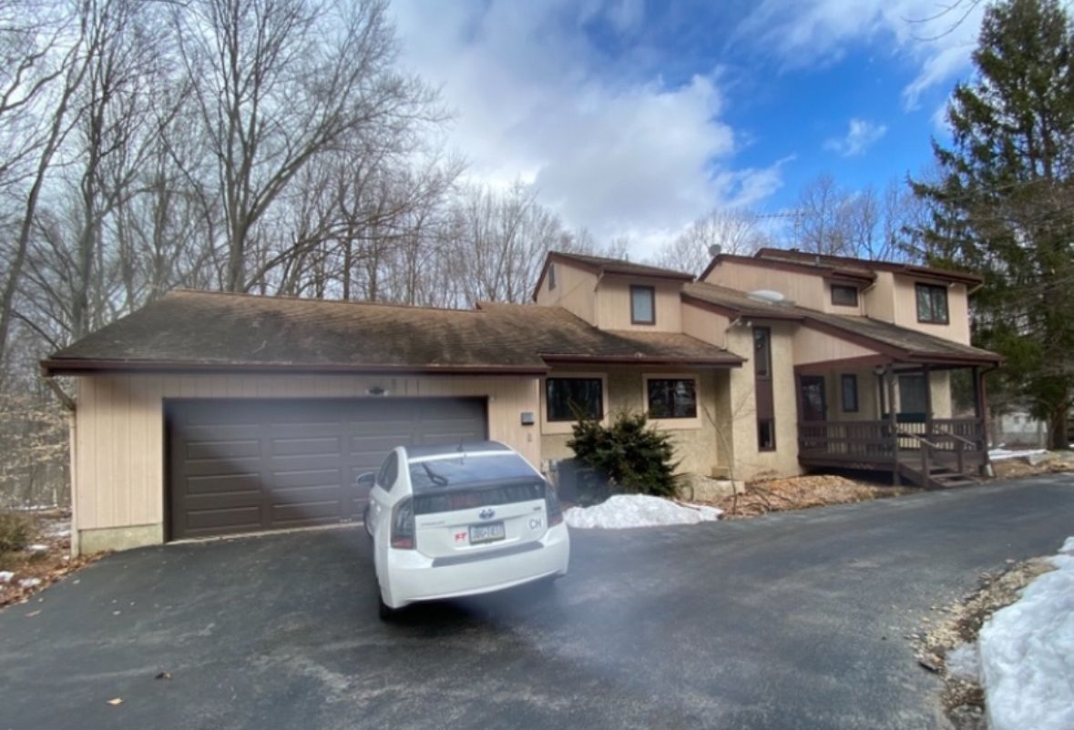 A white car is parked in front of a large house.