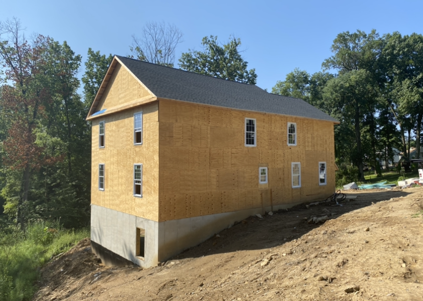 A large house is being built on top of a dirt hill.