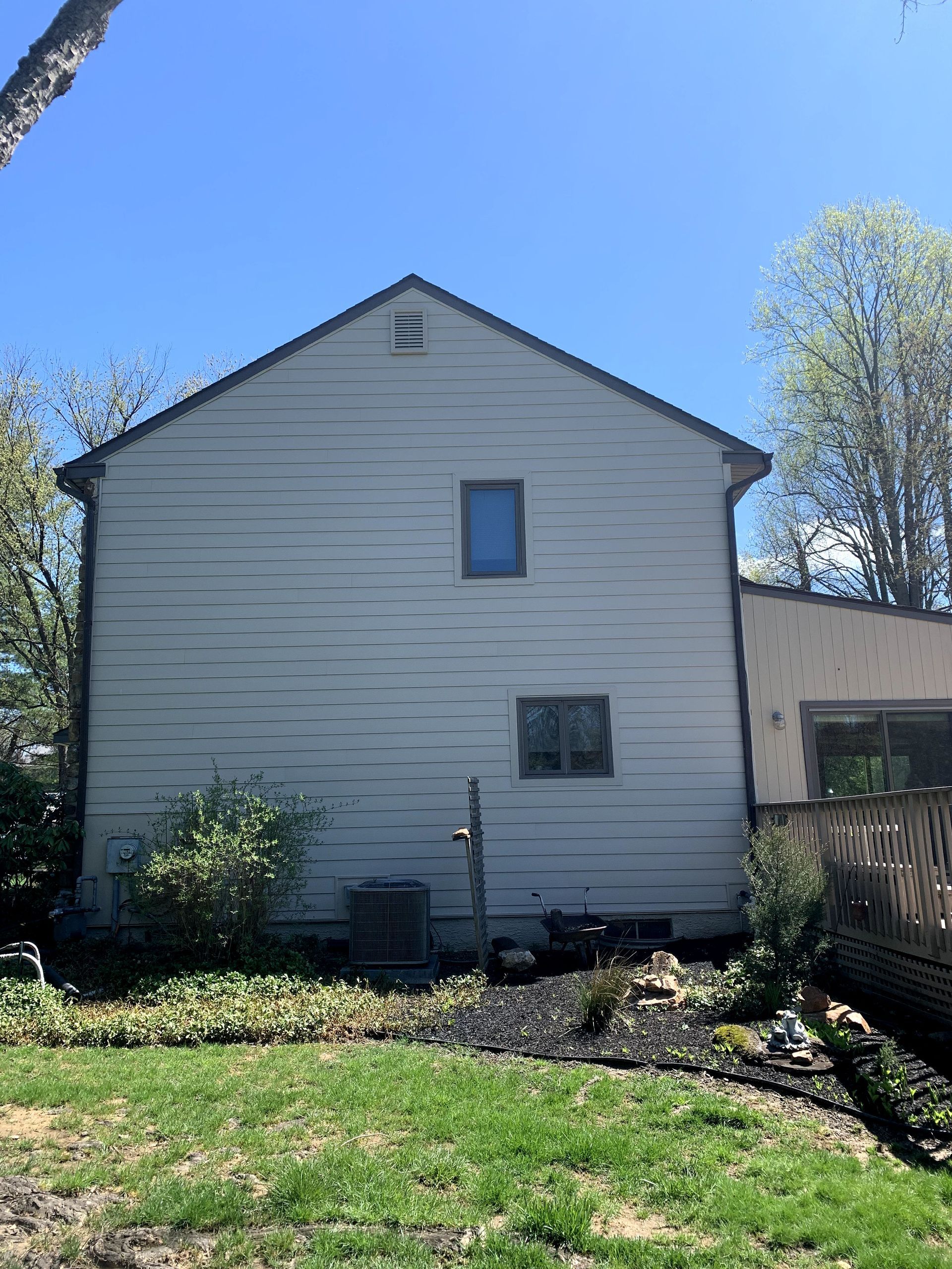 A large white house with a lot of windows is sitting in the middle of a lush green yard.