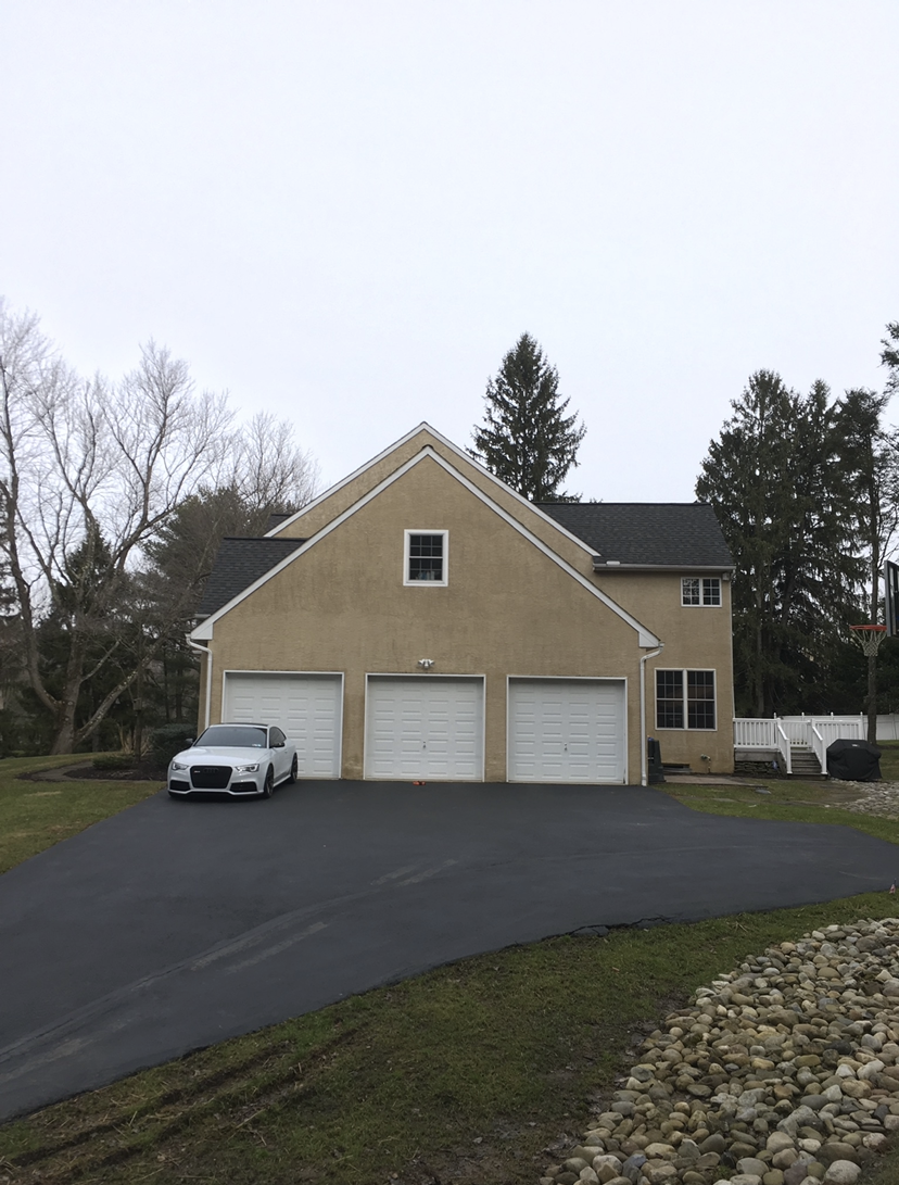 A car is parked in front of a large house with three garage doors.