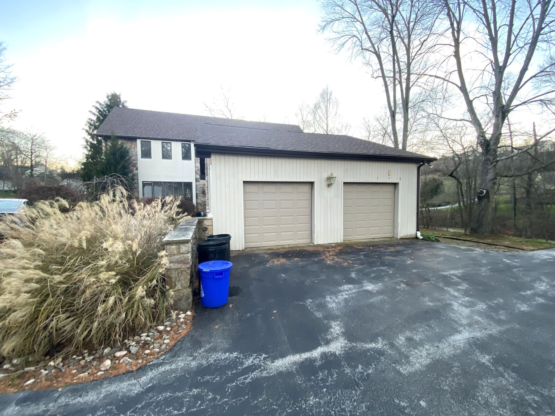 A garage with two garage doors and a blue trash can in front of it.