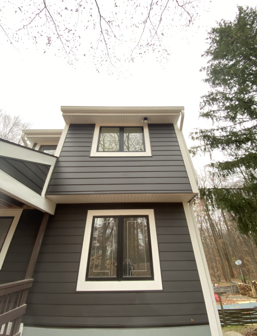 The front of a house with a black siding and white trim.